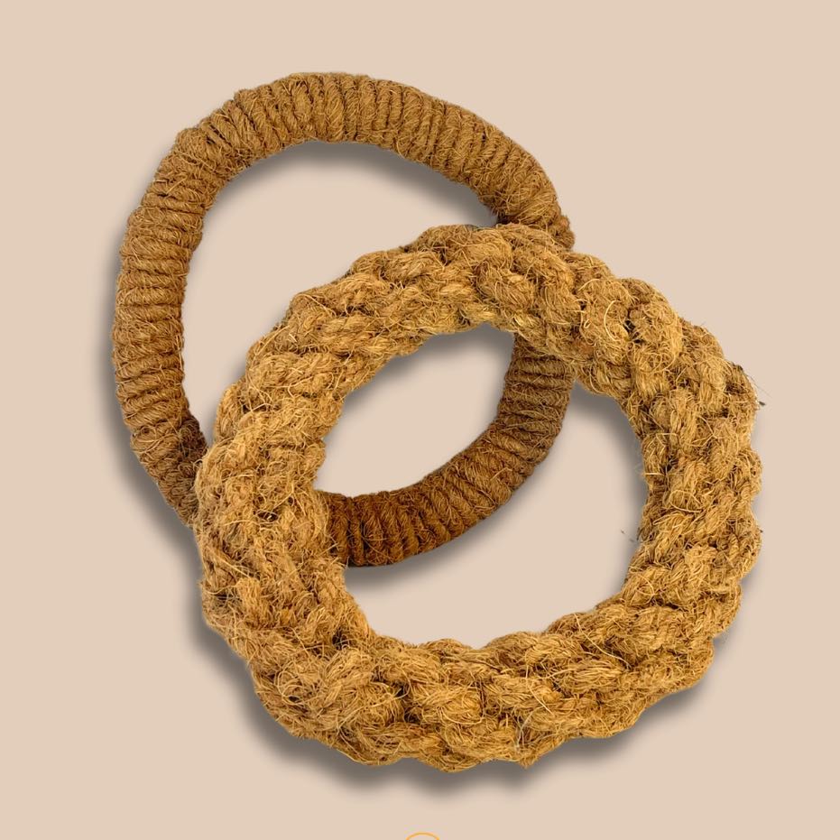Two woven, coconut fiber dog tug toy rings on a beige background.