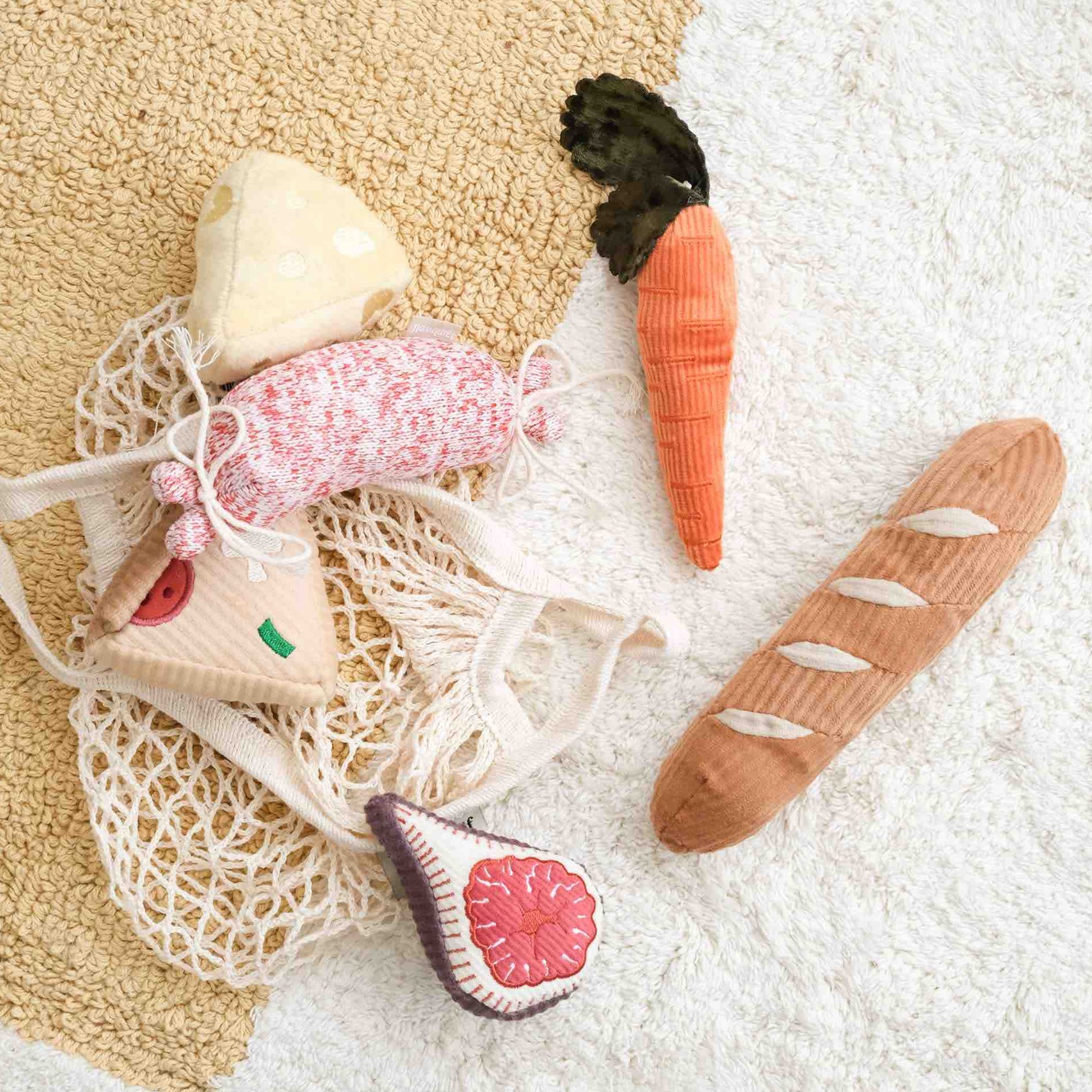 Plush dog toys resembling a carrot, bread, pizza, cheese and fig on a textured surface.