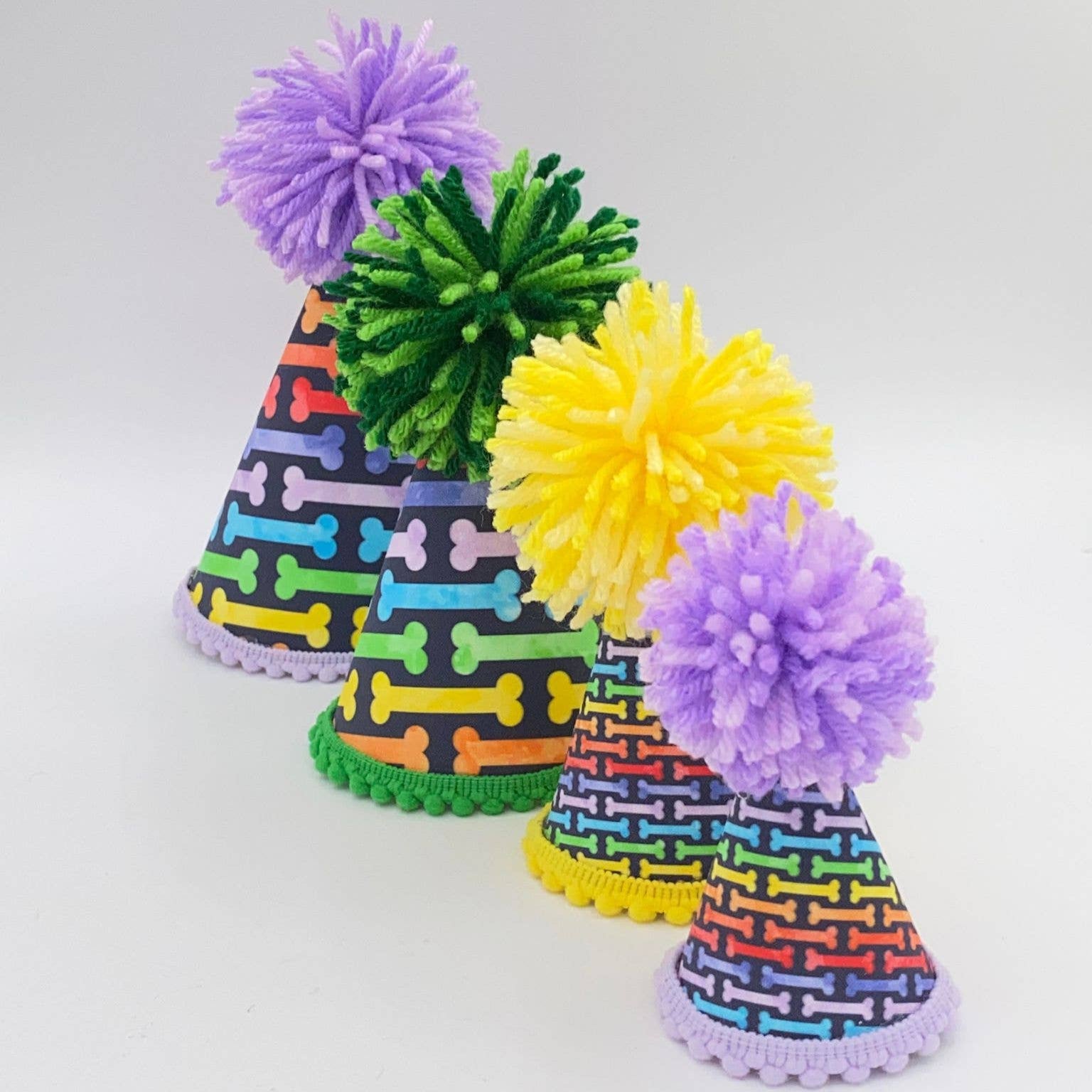 An array of dog party hats adorned with rainbow bones and colored pom-poms on top.