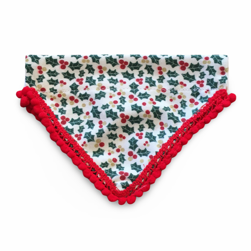 A large white dog bandana with a holly and berries print, trimmed with red pompoms.