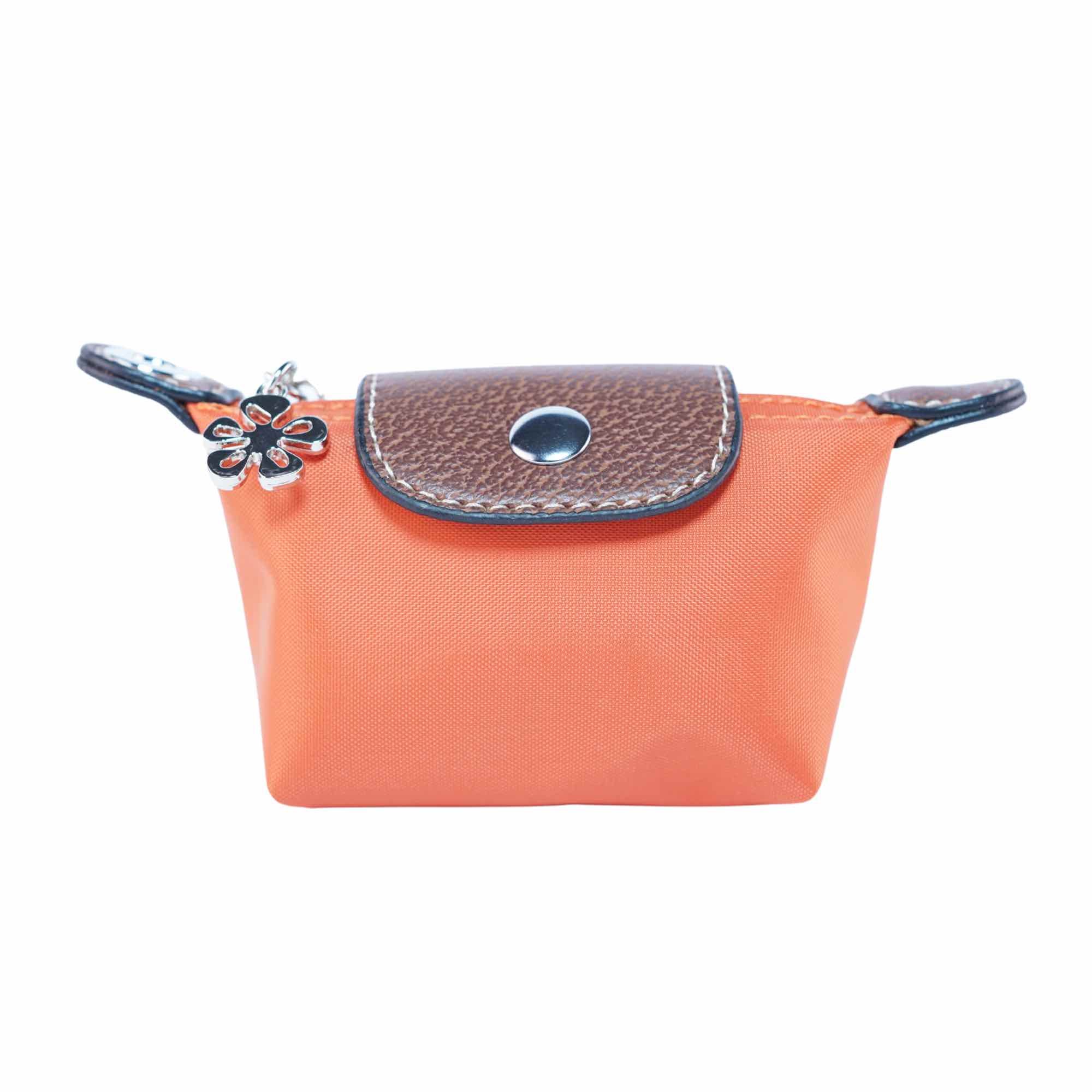 Small orange dog waste bag pouch with brown leather flap and flower charm on a white background.