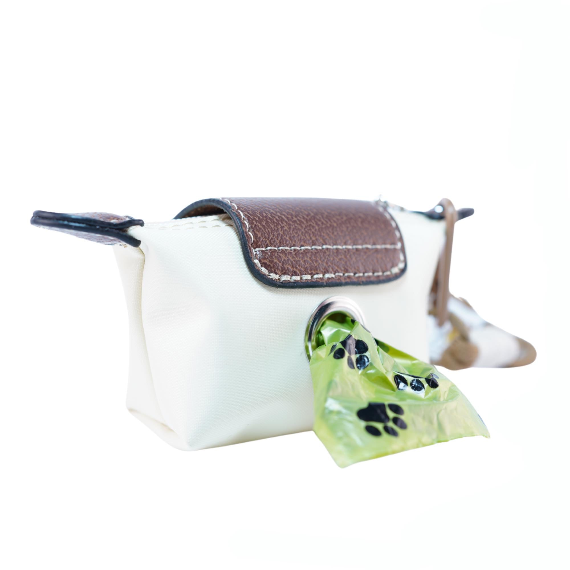Small white dog waste bag pouch with brown leather flap and bag protruding from dispensing hole on a white background.