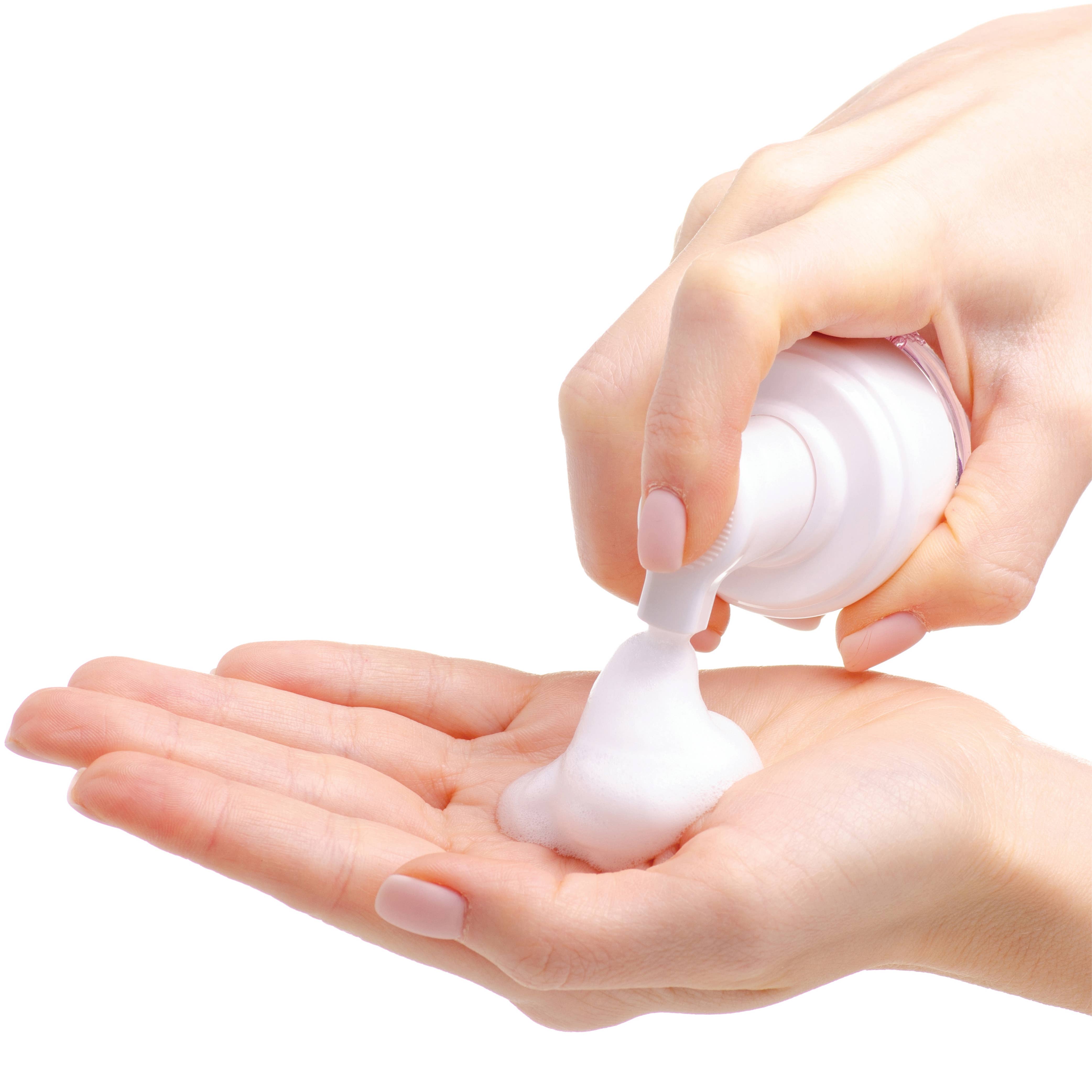 Hand squeezing a small white bottle of cream onto another hand against a white background.