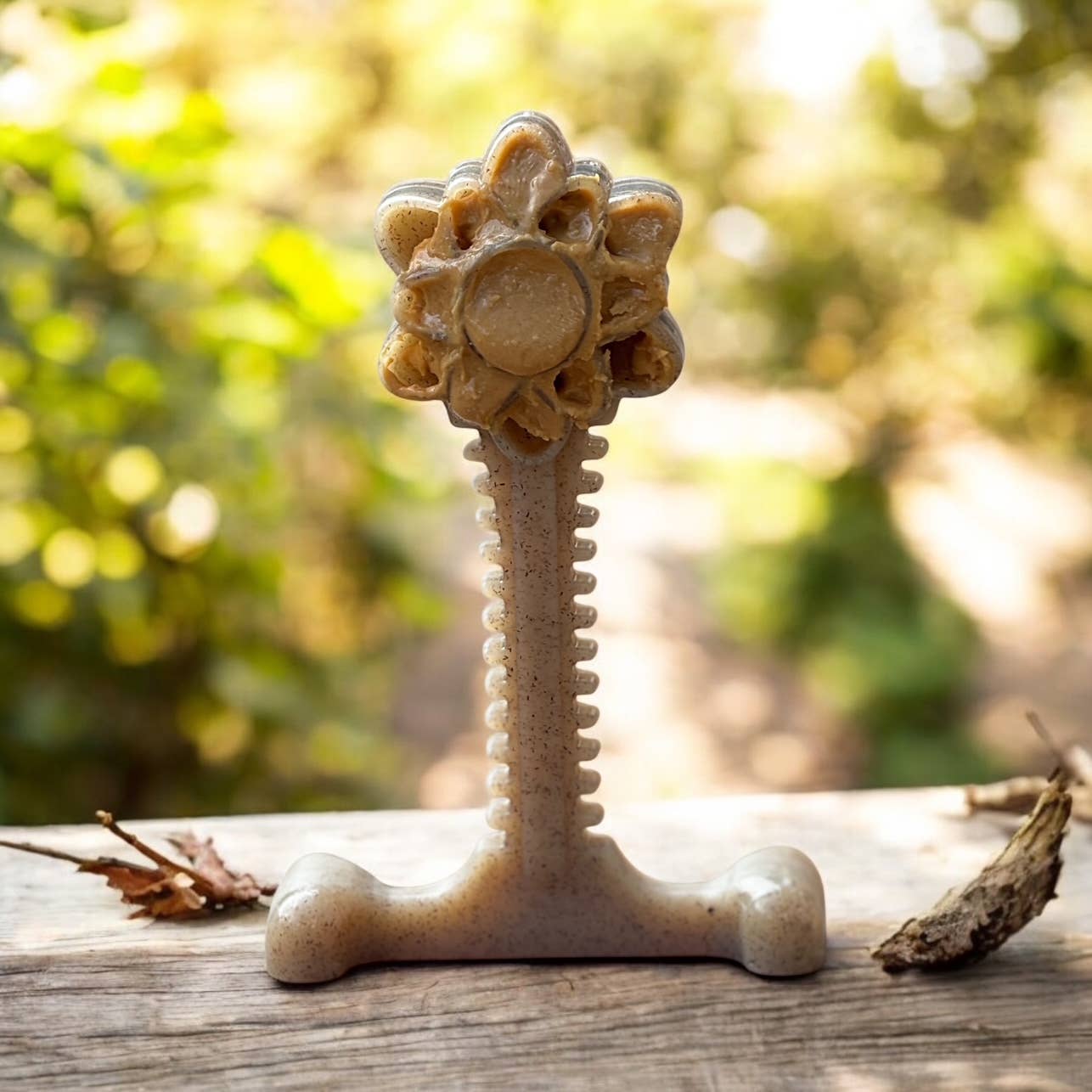 SodaPup's beige Honey Bone Flower Tower dog toy standing on a wood table with peanut butter smeared into it for licky fun.