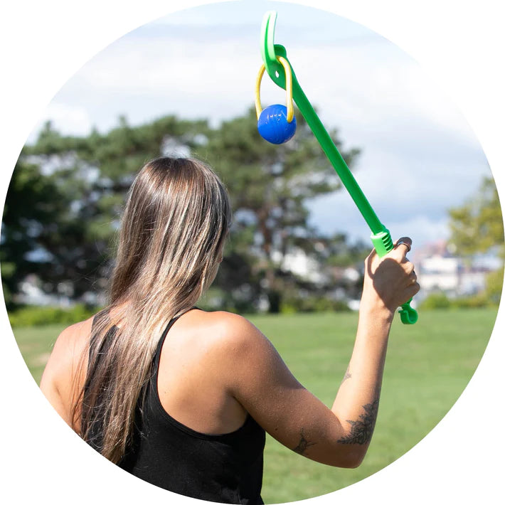 A woman in a park preparing to launch a ball for her dog to fetch.