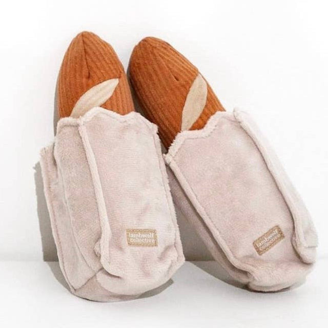 A plush dog toy shaped like a baguette with a crinkly paper bag attached, in shades of beige and brown.