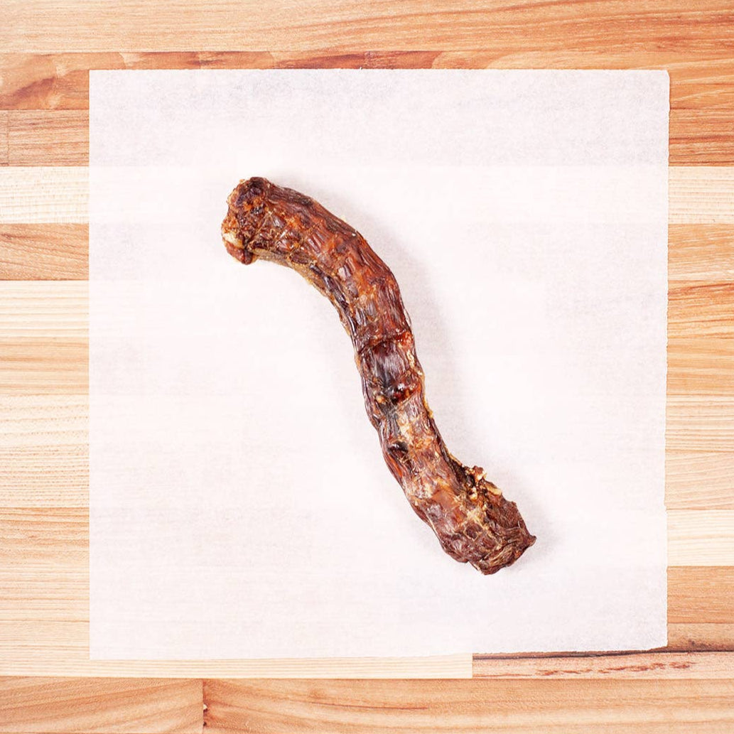 A duck neck dog chew on white paper on a cutting board.