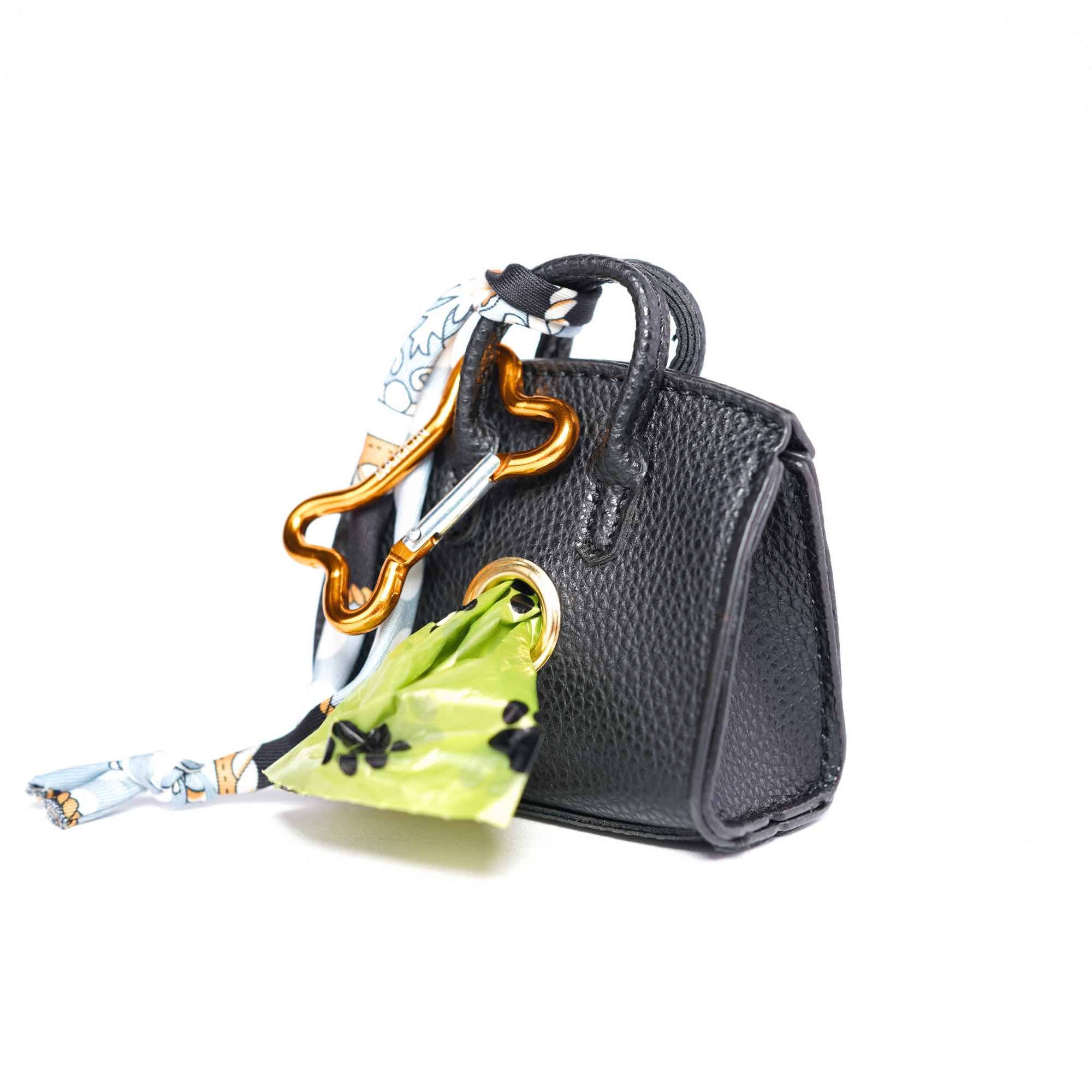 Black handbag-style dog waste bag holder with bone-shaped carabiner on a white background.